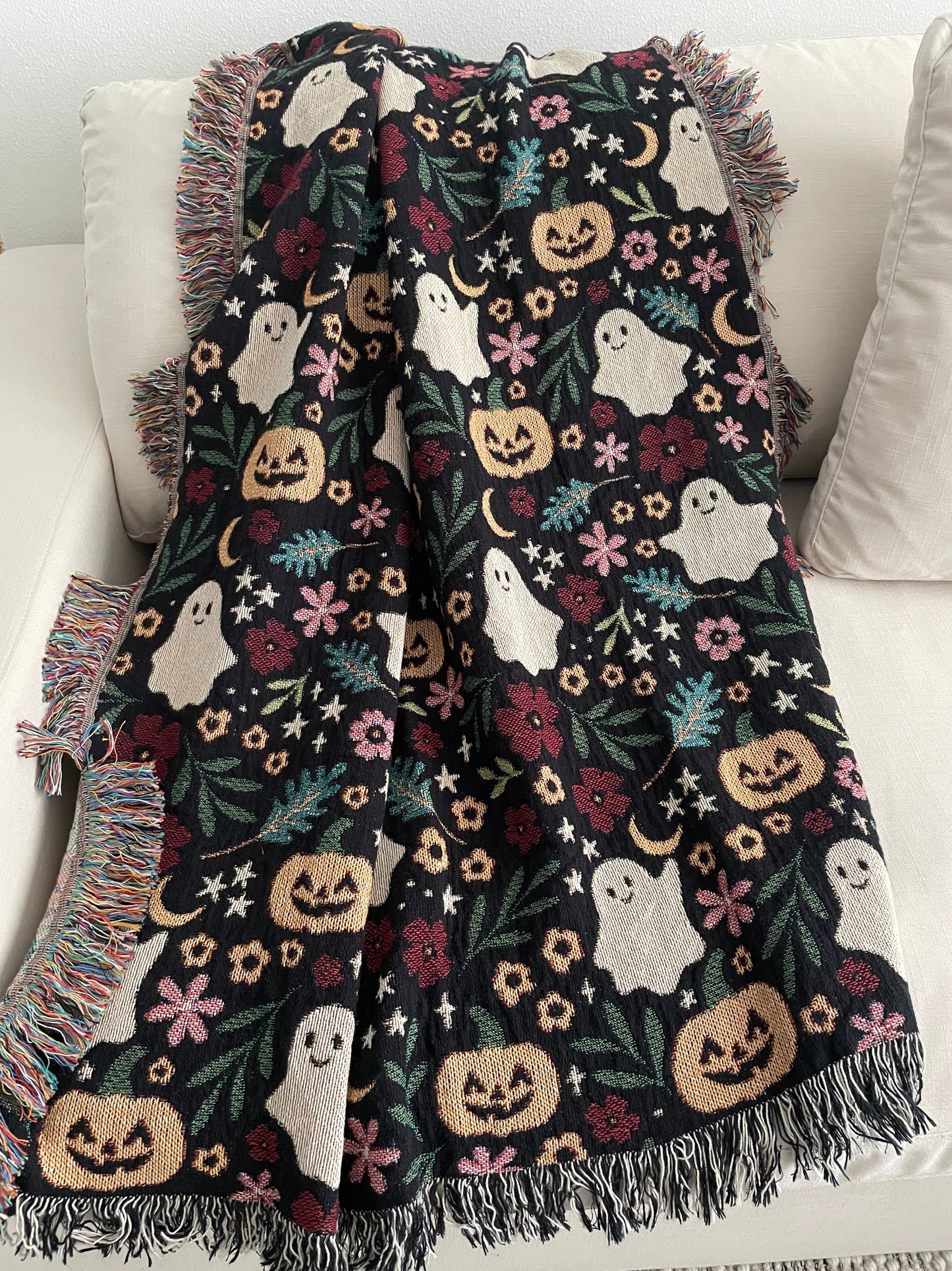 Halloween-themed blanket with ghosts, pumpkins, and crescent moons, and stars draped over a couch.