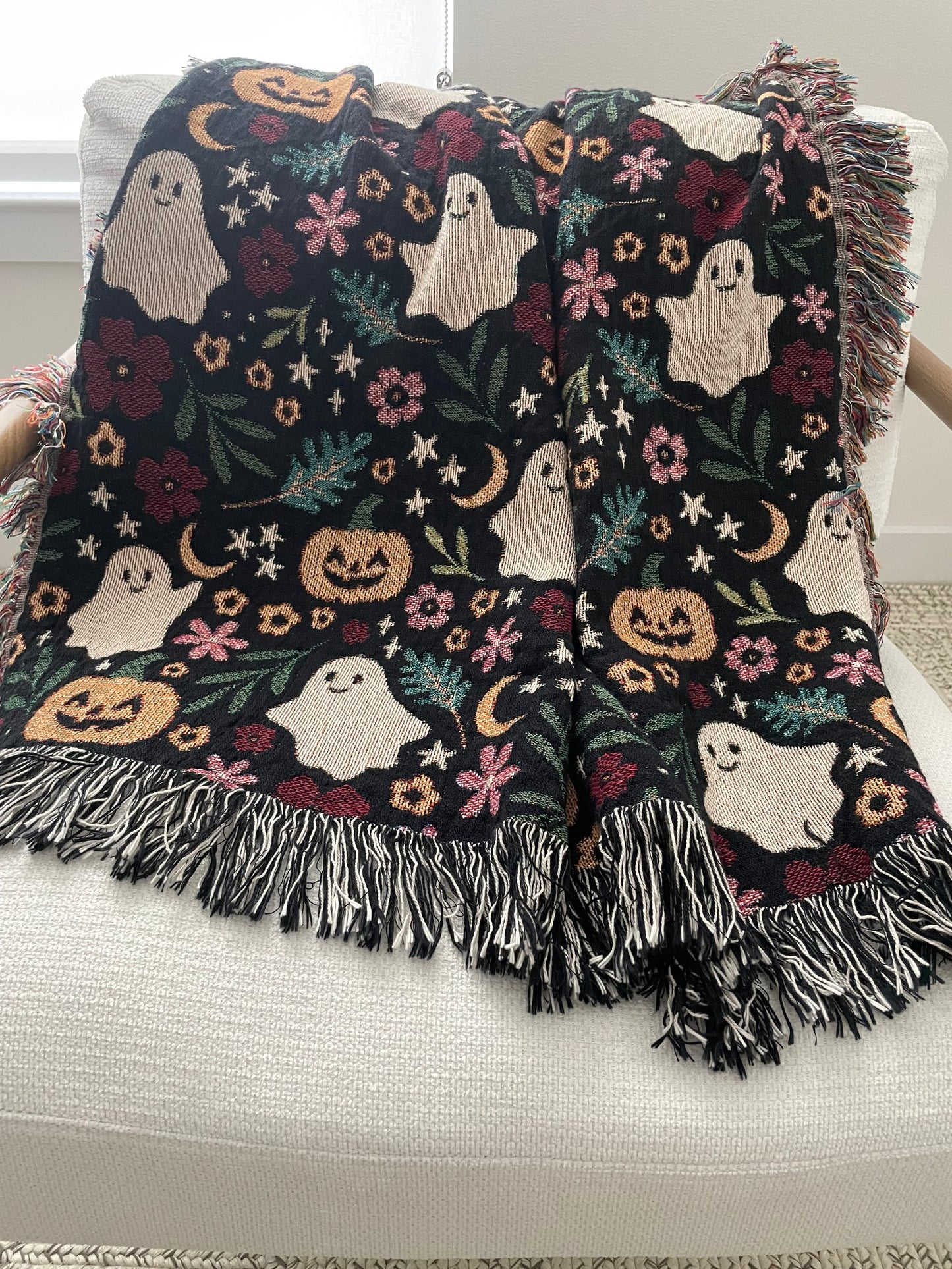 Halloween-themed blanket with ghosts, pumpkins, and flowers draped over a chair.