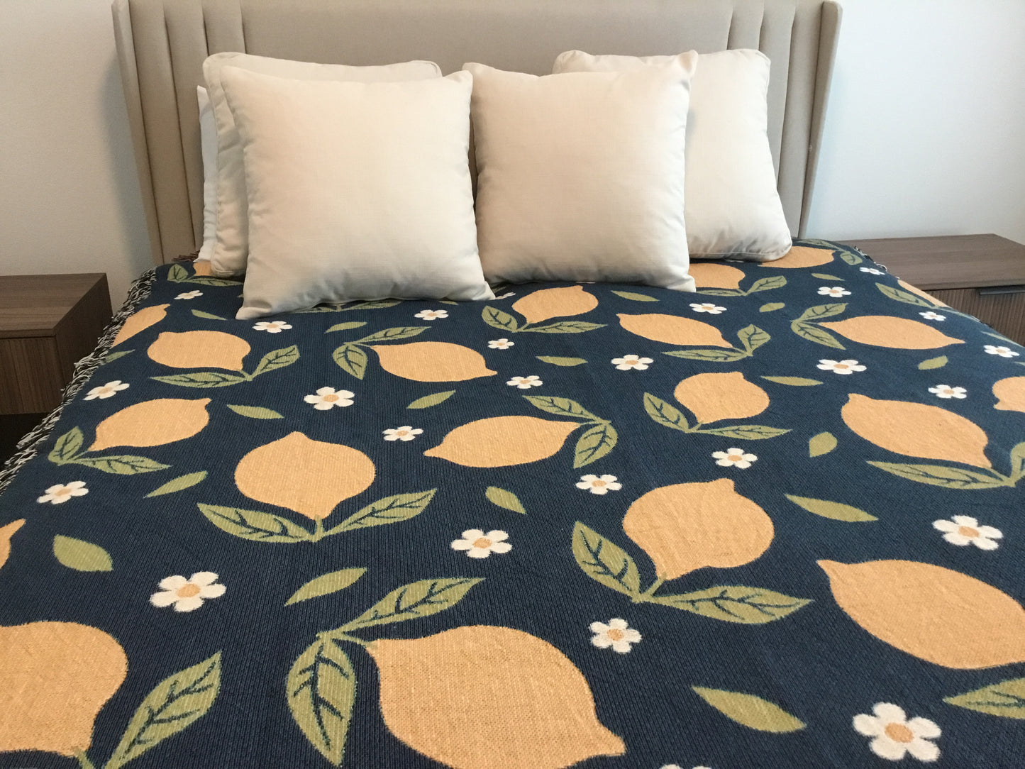 Lemon and daisy patterned woven throw blanket in navy, styled as a bed topper on a queen bed.