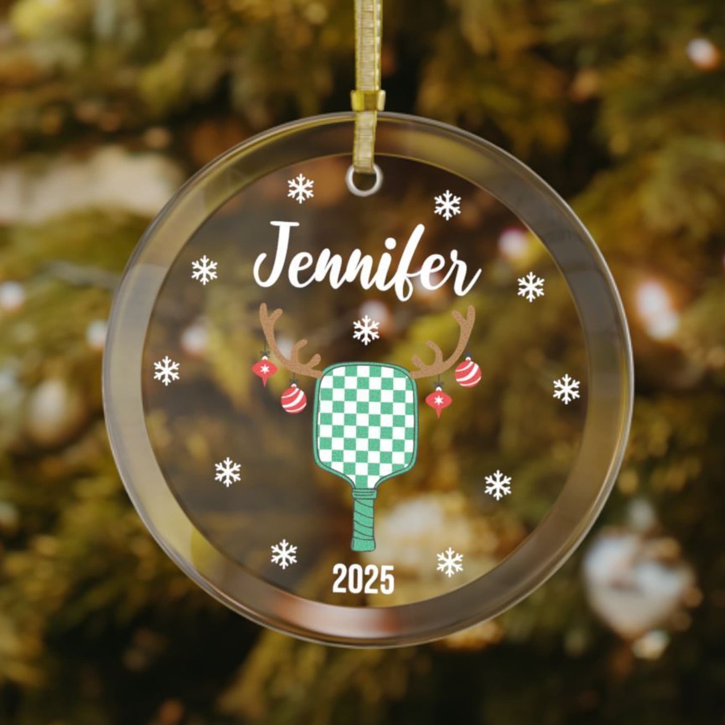 Personalized pickleball Christmas ornament featuring a green checkered paddle with antlers having ornaments, snowflakes around the design, and customized name on top and year on bottom.