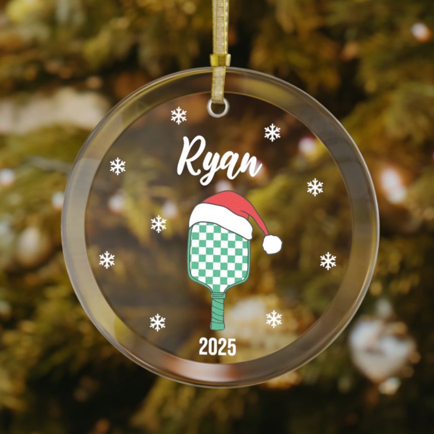 Personalized pickleball Christmas ornament featuring a green checkered paddle wearing a Santa hat, snowflakes around the design, and customized name on top and year on bottom.