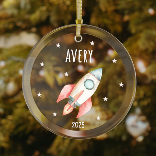 Personalized rocket ship Christmas glass ornament with custom name and year, featuring a red, white, and navy rocket and silver stars. A fun holiday gift for space-loving kids and teens.