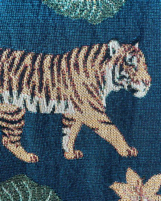 Close-up of a woven tiger throw blanket showing the detailed jacquard weave, walking tiger design, and dark teal-blue background.
