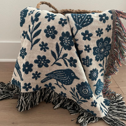 Floral and bird patterned throw blanket with fringed edges.