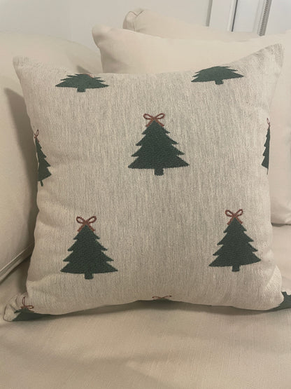 Beige woven Christmas throw pillow with green Christmas tree pattern and red bow accents, styled on a sofa for cozy holiday décor.