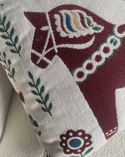 A close-up of a woven throw pillow featuring a traditional Swedish horse design.
