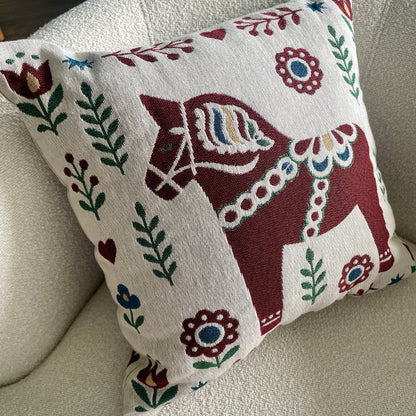 A 17x18 throw pillow with a traditional Swedish Dala horse design, resting on a textured cream-colored armchair.
