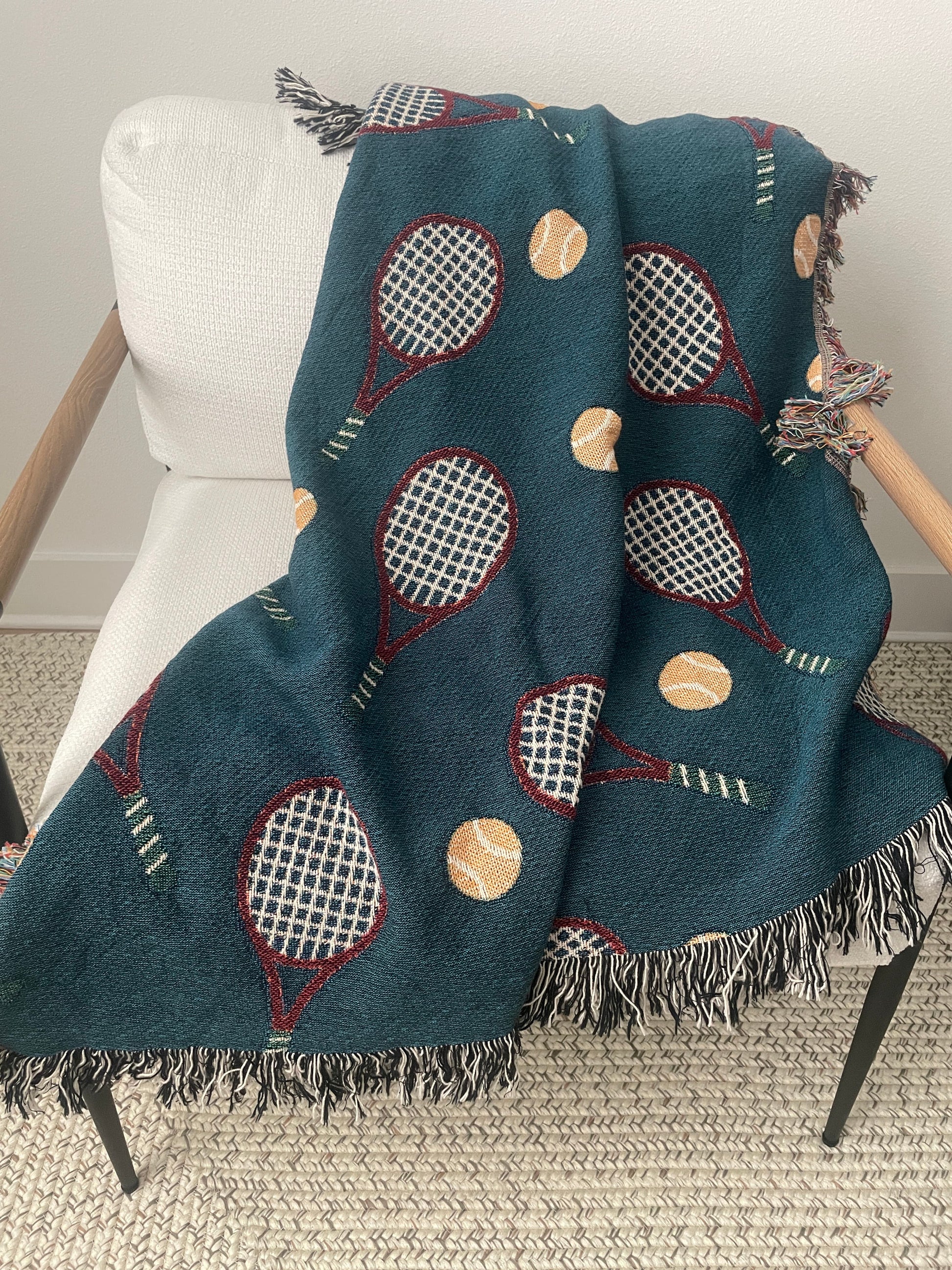 Dark teal tennis racket woven throw blanket with fringe draped over a chair.