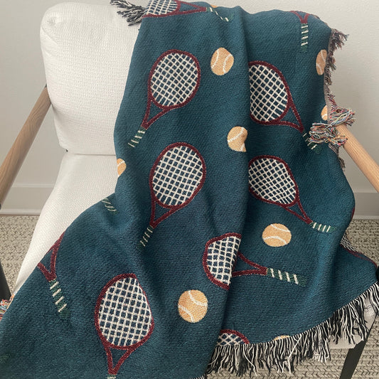 Dark teal tennis racket woven throw blanket with fringe draped over a chair.