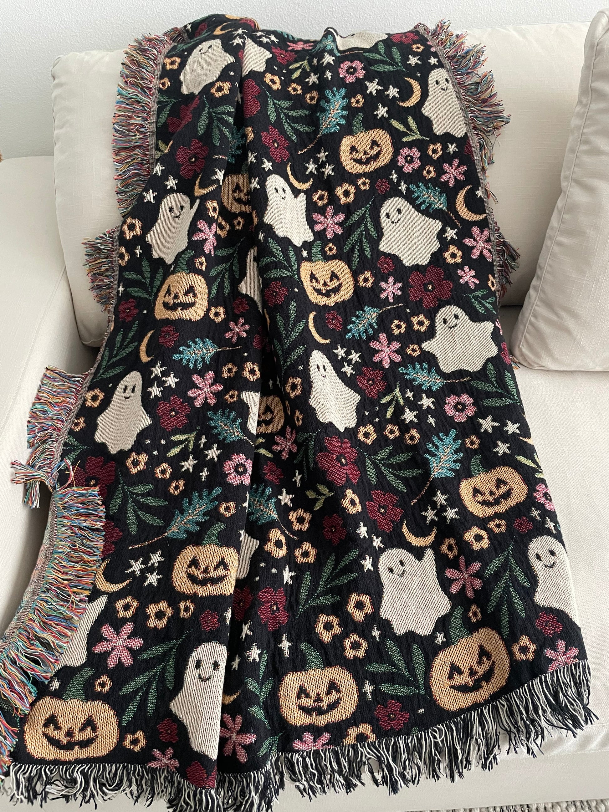 Halloween-themed blanket with ghosts, pumpkins, and crescent moons, and stars draped over a couch.