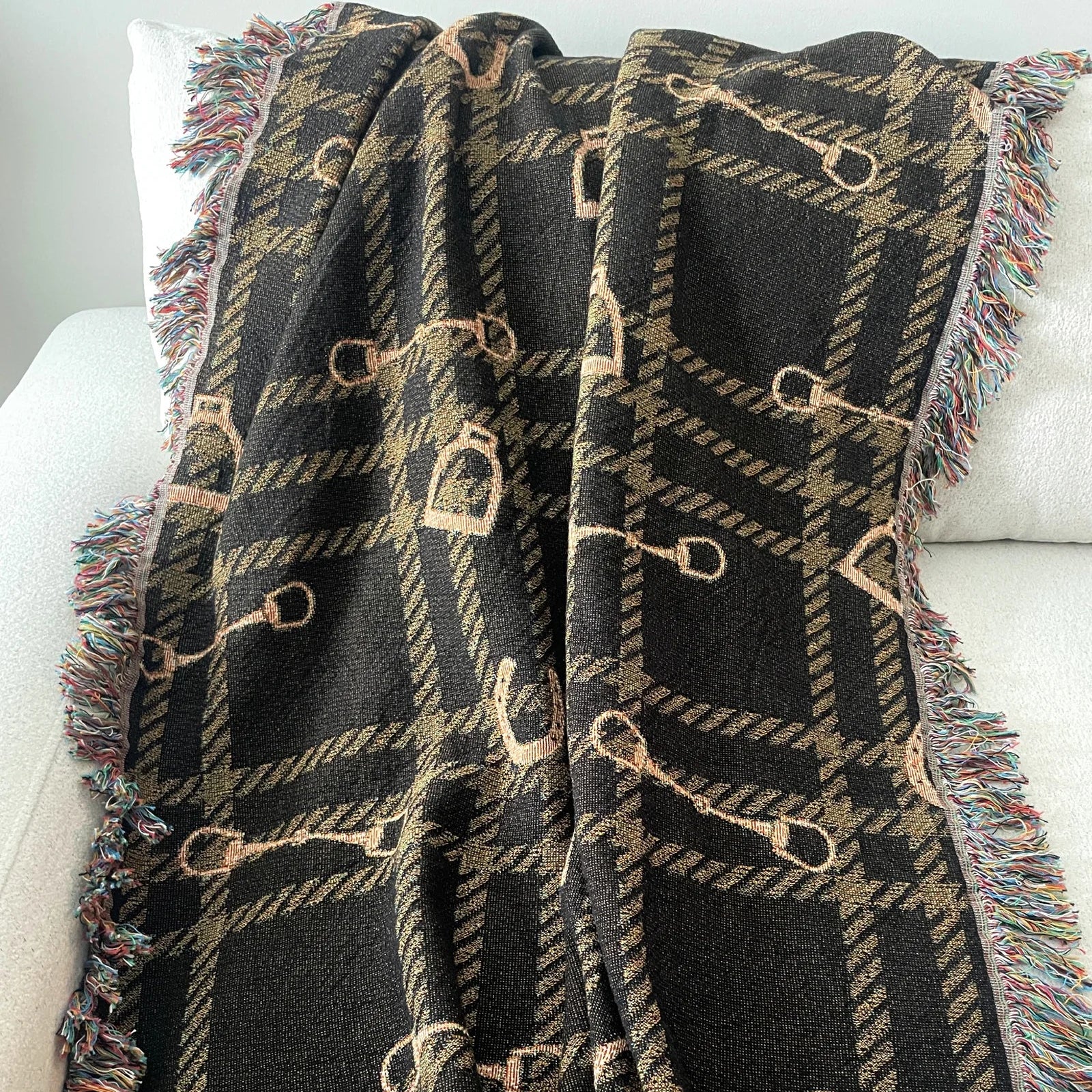 Horse bit plaid woven blanket in dark brown and gold tones, jacquard-woven 100% cotton equestrian throw with fringe edges, styled over a white sofa for classic horse-inspired home decor.