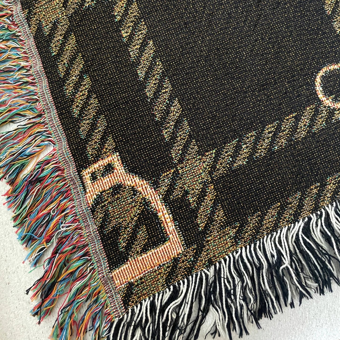 Close-up detail of horse bit plaid woven blanket in dark brown and gold, jacquard-woven 100% cotton equestrian throw with multicolored and black and white fringe edges.