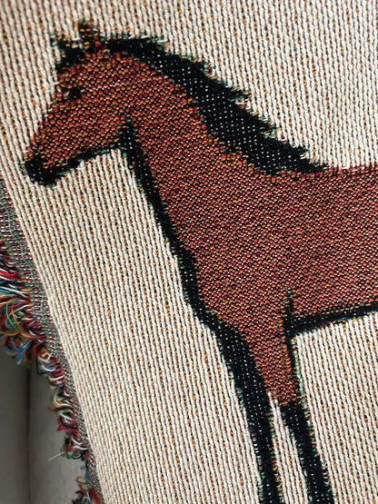 Close-up detail of jacquard-woven cotton horse motif blanket showing textured weave, rich earthy tones, and multicolored fringe edge for classic equestrian home decor.