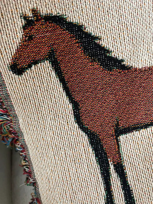 Close-up detail of jacquard-woven cotton horse motif blanket showing textured weave, rich earthy tones, and multicolored fringe edge for classic equestrian home decor.