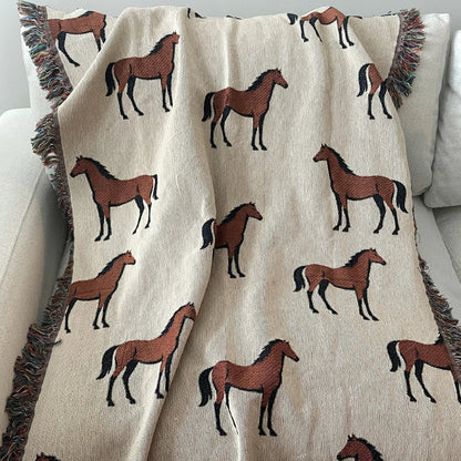 Horse motif woven blanket made from 100% cotton jacquard, featuring repeating chestnut horses on a neutral background with fringe edges, styled on a sofa for classic equestrian home decor.