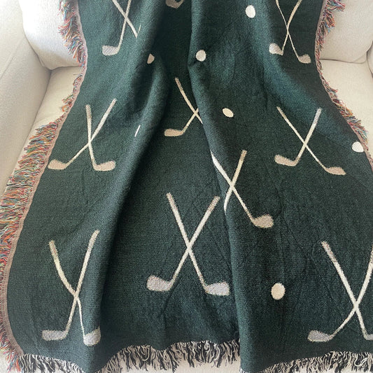 Golf clubs woven throw blanket in forest green, jacquard woven cotton with crossed golf club and golf ball pattern, draped over a chair