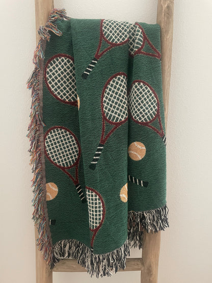 Green tennis racket woven throw blanket with fringe displayed on a wooden ladder.
