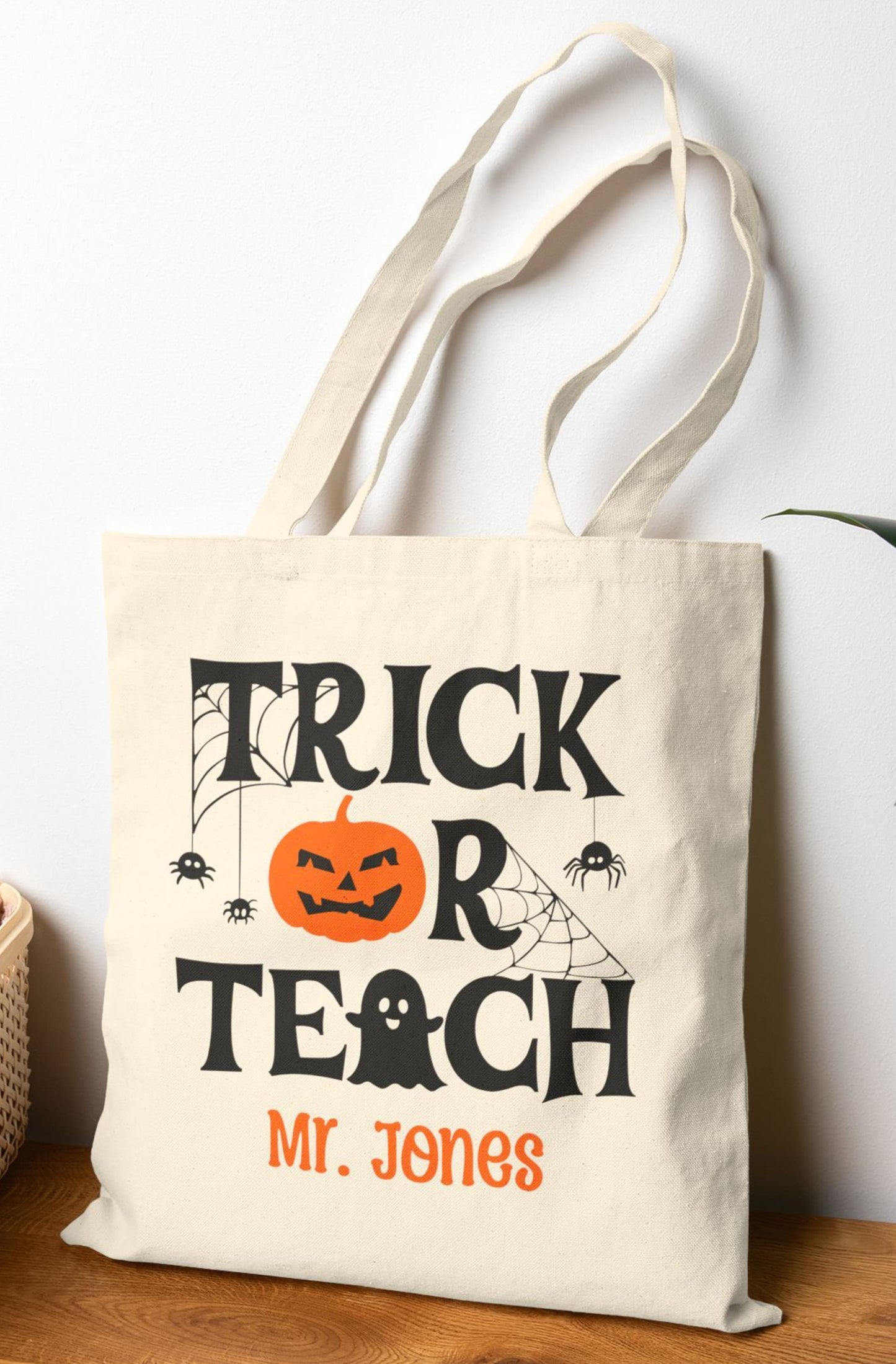 Custom Halloween tote bag for teachers featuring 'Trick or Teach' phrase with ghost, jack-o'-lantern, spider webs, and personalized name on canvas bag.