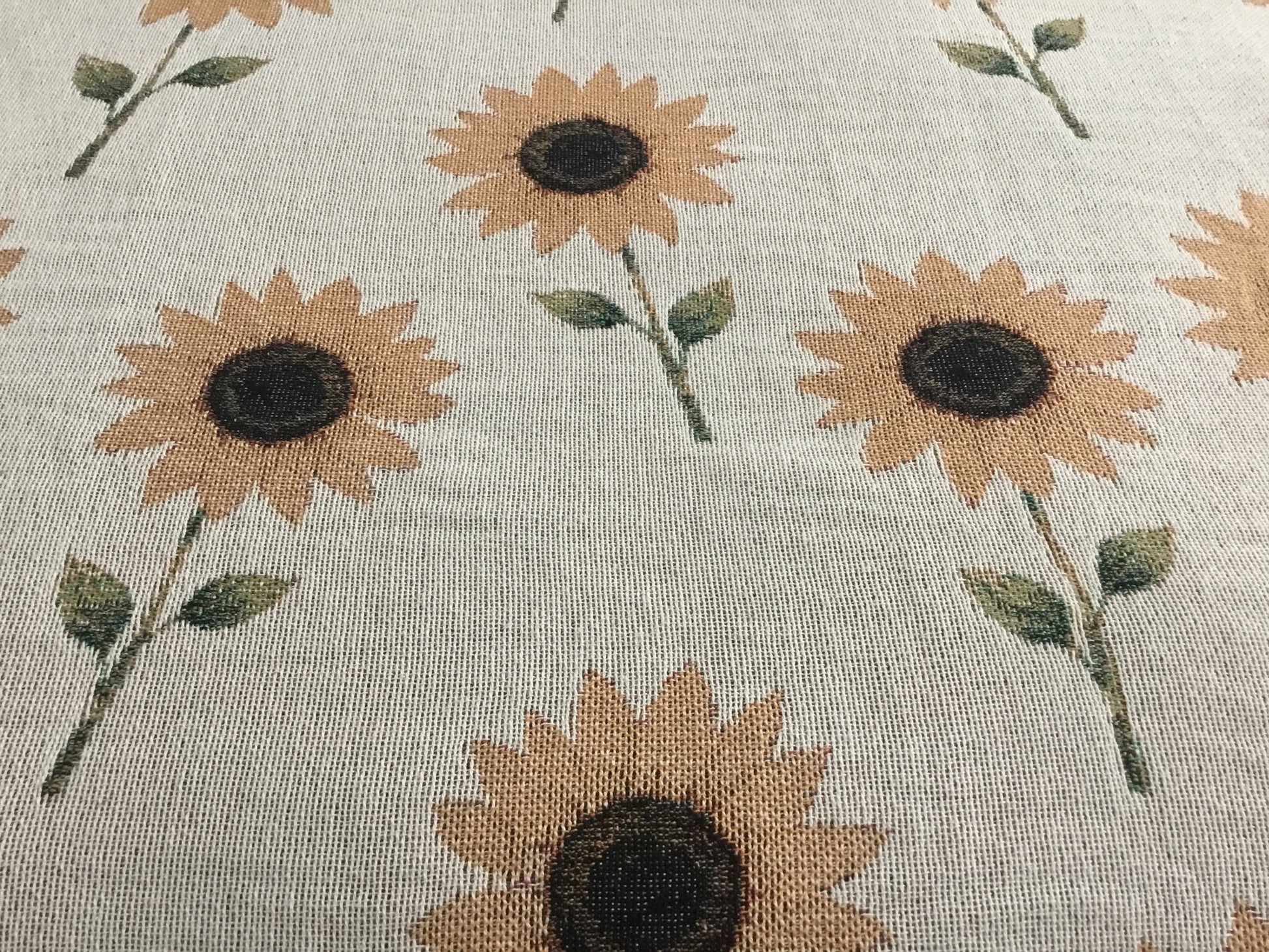 Close-up of a beige woven throw blanket featuring a repeating pattern of sunflower plants, highlighting the detailed woven texture of the fabric.