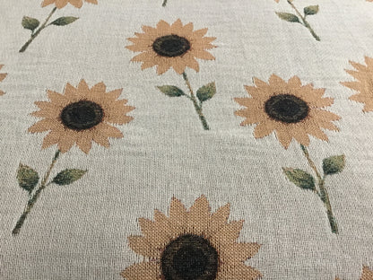 Close-up of a beige woven throw blanket featuring a repeating pattern of sunflower plants, highlighting the detailed woven texture of the fabric.
